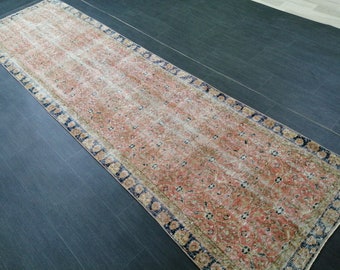 May include: A long, rectangular rug with a faded, vintage appearance. The rug features a central field of muted peach and brown tones with a floral pattern. A dark blue border with floral motifs frames the rug.