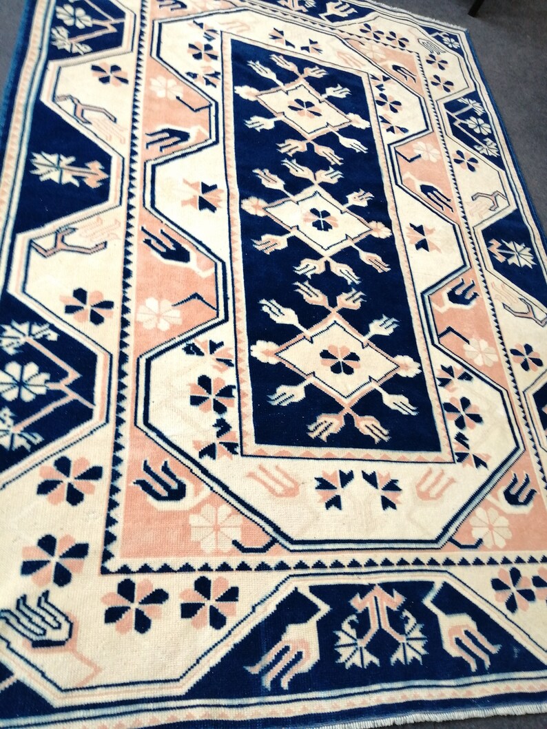 May include: A rectangular rug with a central navy blue panel featuring floral and geometric patterns. The rug has a cream-colored background with pink and navy blue borders and accents. The rug's design includes stylized floral and geometric motifs.