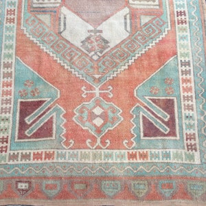 Puede incluir: Una alfombra rectangular de estilo vintage con aspecto envejecido. La alfombra presenta un dise&ntilde;o central en tonos melocot&oacute;n, turquesa y burdeos, con patrones geom&eacute;tricos y un borde. Las dimensiones de la alfombra no son visibles.