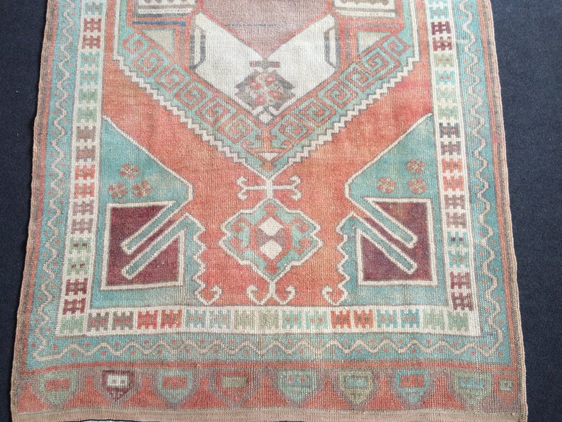 Puede incluir: Una alfombra rectangular de estilo vintage con aspecto envejecido. La alfombra presenta un dise&ntilde;o central en tonos melocot&oacute;n, turquesa y burdeos, con patrones geom&eacute;tricos y un borde. Las dimensiones de la alfombra no son visibles.
