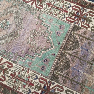 May include: A rectangular, vintage-style rug with a patchwork design. The rug features a palette of muted colours, including brown, purple, and teal. Geometric and floral patterns are visible throughout the rug's surface, creating a textured appearance. The rug has a distressed, antique look.