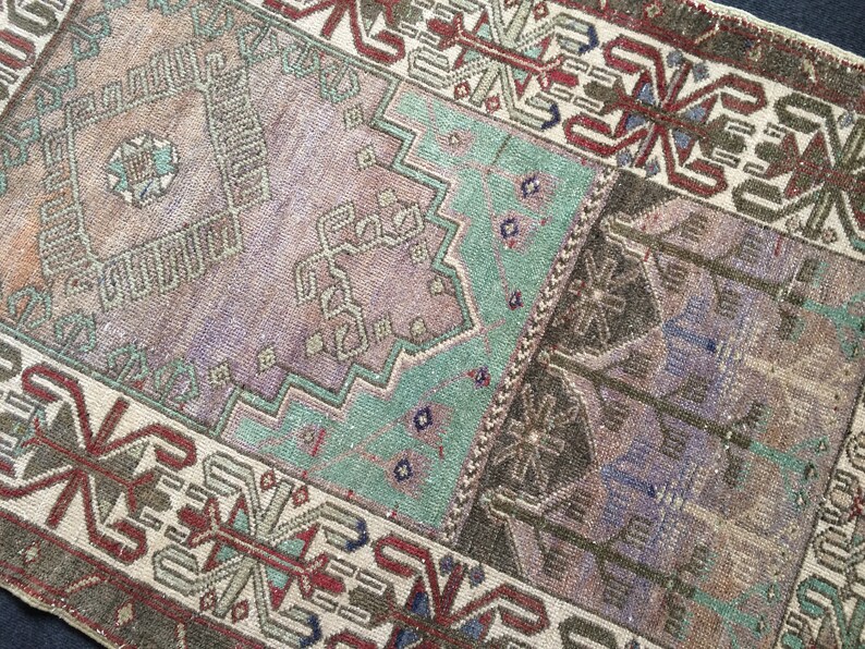 May include: A rectangular, vintage-style rug with a patchwork design. The rug features a palette of muted colours, including brown, purple, and teal. Geometric and floral patterns are visible throughout the rug's surface, creating a textured appearance. The rug has a distressed, antique look.