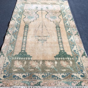 May include: A rectangular, vintage-style rug with a central design featuring an archway and geometric patterns in shades of peach, green, and blue. The rug has a distressed look with a fringed edge, suitable for home decor.