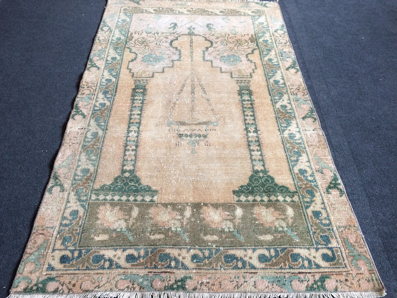 May include: A rectangular, vintage-style rug with a central design featuring an archway and geometric patterns in shades of peach, green, and blue. The rug has a distressed look with a fringed edge, suitable for home decor.