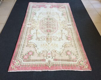 Puede incluir: Alfombra rectangular con un campo central crema con un diseño floral en rosa y beige. La alfombra tiene un borde rosa y está colocada sobre una superficie oscura. El diseño de la alfombra incluye motivos florales y de desplazamiento.
