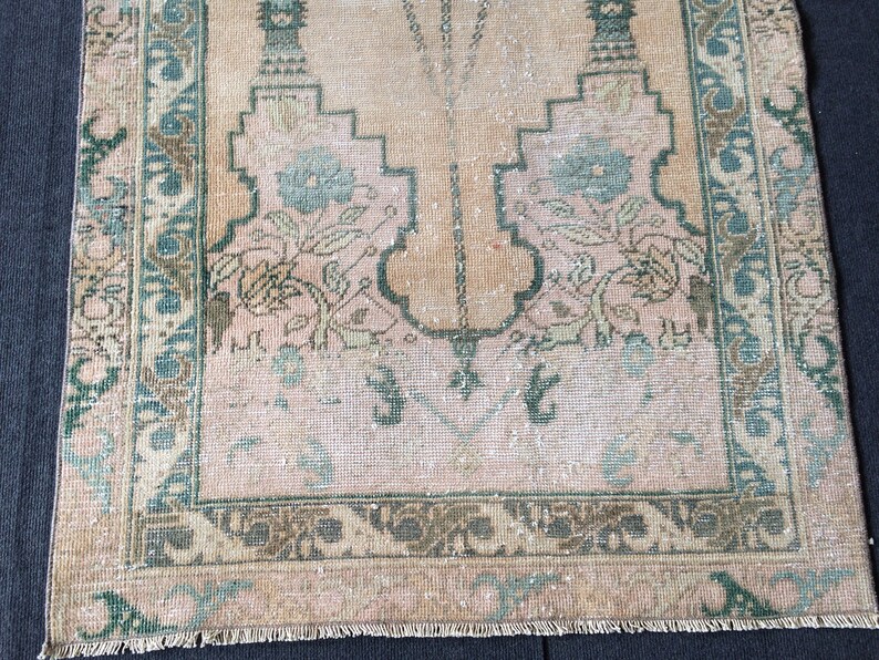 May include: A vintage rug with a central design in shades of peach and beige, framed by a border of teal and brown. The rug features floral motifs and geometric patterns, showcasing a distressed, antique aesthetic.