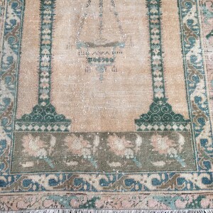 May include: A vintage-style rug with a central design and border. The rug features a beige background with green and blue accents. The border has floral and geometric patterns. The rug's dimensions are not visible in the image.