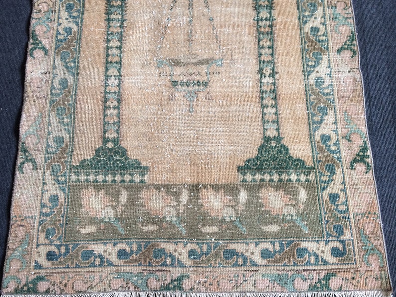 May include: A vintage-style rug with a central design and border. The rug features a beige background with green and blue accents. The border has floral and geometric patterns. The rug's dimensions are not visible in the image.