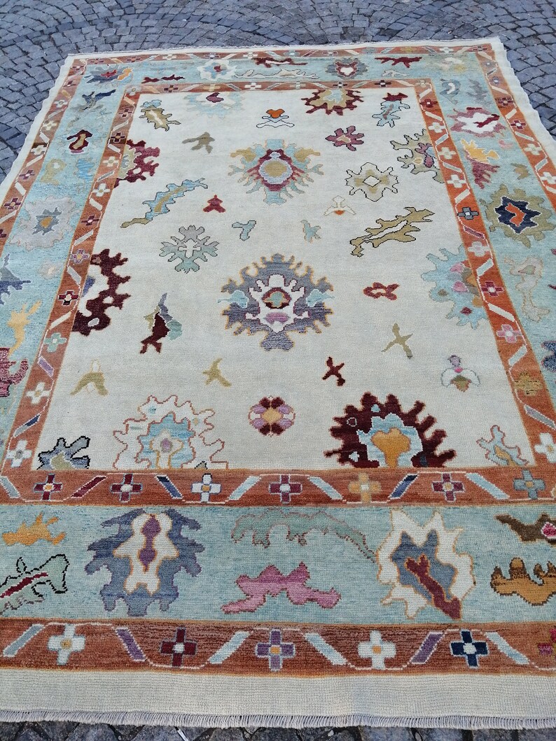 May include: A large, rectangular area rug with an intricate floral pattern. The rug features a cream-colored central field with scattered floral motifs in shades of blue, burgundy, and gold. A border of light blue and rust-colored bands frames the design.