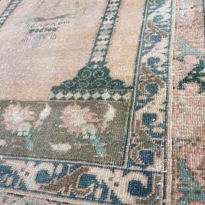 May include: A vintage rug with a central peach field and a dark green border. The border features a repeating geometric pattern in teal and brown. The rug has a distressed appearance, with faded colors and visible wear.