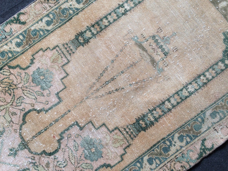 May include: A rectangular, vintage-style rug with a faded, distressed appearance. The rug features a central field in a warm beige hue, framed by a border of teal and pink floral patterns. The design includes geometric shapes and floral motifs.