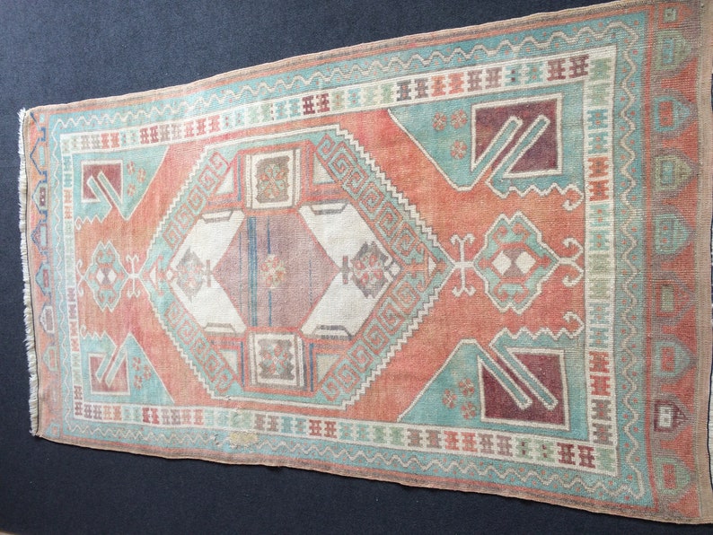 Puede incluir: Alfombra rectangular de estilo vintage con aspecto desgastado. Presenta un dise&ntilde;o central de rombos en tonos melocot&oacute;n, turquesa y burdeos, enmarcado por bordes geom&eacute;tricos. Flecos en los extremos cortos acent&uacute;an su est&eacute;tica envejecida.