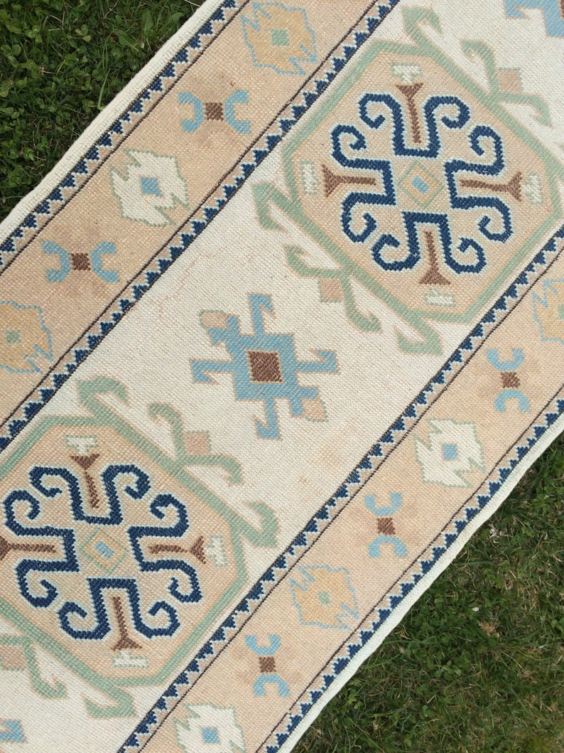 May include: A rectangular rug with a cream-colored central field and intricate geometric patterns. The border features a tan hue with blue, green, and brown accents. The rug's design includes stylized floral and geometric motifs, creating a traditional aesthetic.