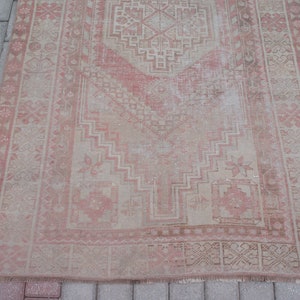 May include: A rectangular, distressed rug with a faded, vintage appearance. The rug features a central geometric design in shades of pink and beige, framed by a detailed border. The rug's design includes floral and geometric patterns.