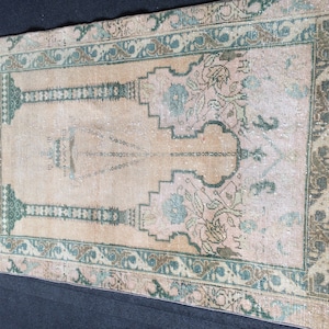 May include: Vintage beige and pink rug with a central design and a decorative border in shades of green and brown. The rug features floral and geometric patterns, adding a touch of elegance to any space. The rug is rectangular in shape.