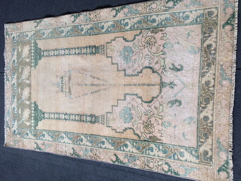 May include: Vintage beige and pink rug with a central design and a decorative border in shades of green and brown. The rug features floral and geometric patterns, adding a touch of elegance to any space. The rug is rectangular in shape.