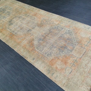 May include: A rectangular, distressed rug with a faded, vintage appearance. The rug features a central design in shades of orange, gray, and beige. The rug's pattern includes geometric shapes and borders, creating a classic, aged aesthetic. The rug is suitable for home decor.