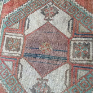 Puede incluir: Primer plano de una alfombra vintage con un patr&oacute;n geom&eacute;trico. La alfombra presenta una forma de diamante central en tonos marrones y blancos, enmarcada por bordes turquesa y naranja. El dise&ntilde;o incluye motivos geom&eacute;tricos repetidos.