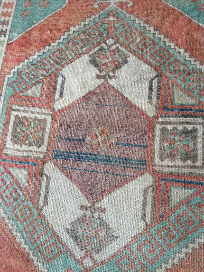 Puede incluir: Primer plano de una alfombra vintage con un patr&oacute;n geom&eacute;trico. La alfombra presenta una forma de diamante central en tonos marrones y blancos, enmarcada por bordes turquesa y naranja. El dise&ntilde;o incluye motivos geom&eacute;tricos repetidos.
