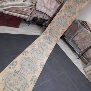 May include: A long, rectangular rug with a peach-colored background and geometric patterns in shades of blue and cream. The rug features a repeating design of octagonal and floral motifs, creating a vintage aesthetic. The rug is displayed on a dark gray tiled floor.