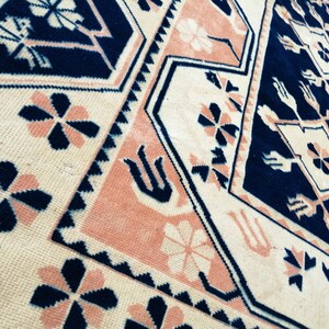 May include: Close-up of a patterned rug with a geometric design. The rug features a cream-colored background with navy blue and peach-colored accents. The design includes floral and geometric shapes.