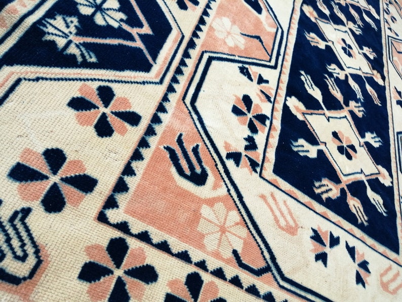 May include: Close-up of a patterned rug with a geometric design. The rug features a cream-colored background with navy blue and peach-colored accents. The design includes floral and geometric shapes.