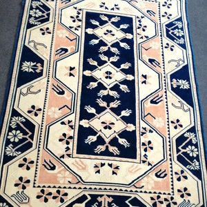 May include: Rectangular rug with a navy blue, cream, and blush pink geometric pattern. The rug features a central navy blue panel with cream and pink floral and geometric designs. The border is navy blue with cream and pink accents.