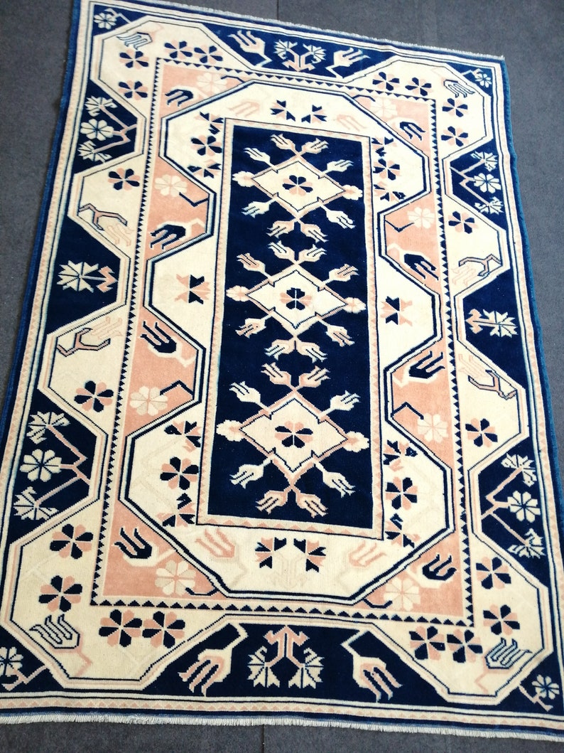 May include: Rectangular rug with a navy blue, cream, and blush pink geometric pattern. The rug features a central navy blue panel with cream and pink floral and geometric designs. The border is navy blue with cream and pink accents.