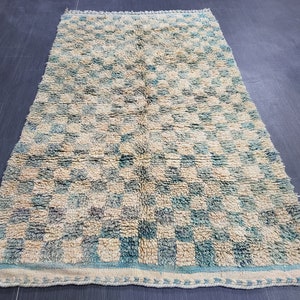 Op de afbeelding: Rechthoekig vloerkleed met een geblokt patroon in beige en turquoise. Het kleed heeft een getextureerde, geweven uitstraling en een lichtere rand. Geschikt voor een woon- of slaapkamer, meet ongeveer 150 cm x 250 cm.