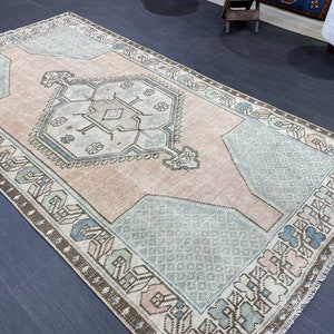 Puede incluir: Una alfombra rectangular de aspecto envejecido con un diseño central de medallón. La paleta de colores de la alfombra incluye rosa claro, azul y marrón. El borde tiene un patrón geométrico y la alfombra parece estar hecha de material tejido.