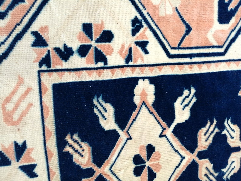 May include: Close-up of a section of a rug with a geometric pattern. The rug features a cream-colored background with navy blue and peach-colored geometric shapes and floral designs. The border is navy blue.