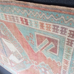 Puede incluir: Primer plano de una alfombra vintage con un patr&oacute;n geom&eacute;trico. La alfombra presenta una combinaci&oacute;n de colores, incluyendo tonos de rojo, turquesa y beige. El dise&ntilde;o incluye formas de diamante y tri&aacute;ngulo, creando una est&eacute;tica tradicional. La textura de la alfombra es visible, sugiriendo una construcci&oacute;n tejida.