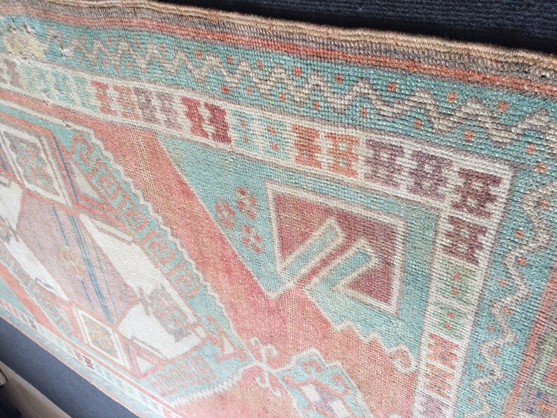 Puede incluir: Primer plano de una alfombra vintage con un patr&oacute;n geom&eacute;trico. La alfombra presenta una combinaci&oacute;n de colores, incluyendo tonos de rojo, turquesa y beige. El dise&ntilde;o incluye formas de diamante y tri&aacute;ngulo, creando una est&eacute;tica tradicional. La textura de la alfombra es visible, sugiriendo una construcci&oacute;n tejida.