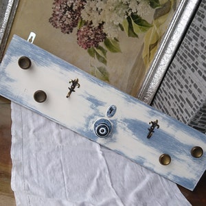 May include: A white and blue painted wooden coat rack with five hooks. The hooks are made of metal and have a decorative design. The rack has a distressed look and is perfect for adding a touch of rustic charm to any home.