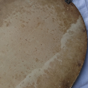 May include: The back of a round, wooden picture frame with a light brown finish. The frame has a metal hanging hook and several small holes around the edge.