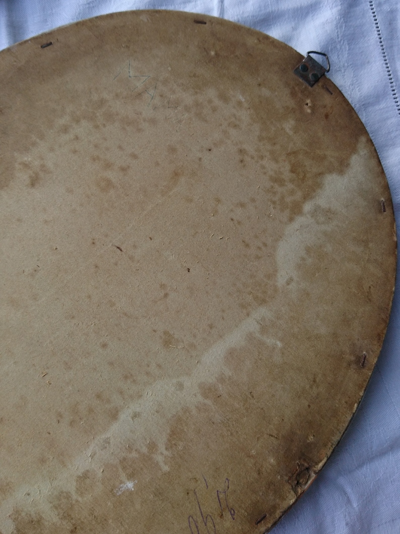 May include: The back of a round, wooden picture frame with a light brown finish. The frame has a metal hanging hook and several small holes around the edge.