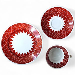 K&ouml;nnte beinhalten: Ein dreiteiliges Keramikgeschirr-Set mit einem rot-wei&szlig;en geometrischen Muster. Das Set umfasst einen gro&szlig;en Teller, eine Untertasse und eine Teetasse. Das Design hat ein sternf&ouml;rmiges Muster in der Mitte.