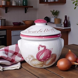 Pode incluir: Pote de cebola de cerâmica branca com borda e tampa rosa, com um desenho de cebola pintado à mão. A tampa tem a palavra "Frivieltorp". Um pano xadrez vermelho e branco e várias cebolas estão por perto.