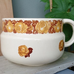 Könnte beinhalten: Ein weißer Keramik-Krug mit braunem und gelbem Blumendesign. Der Krug hat einen großen Henkel und einen runden Körper.