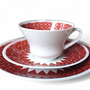 K&ouml;nnte beinhalten: Wei&szlig;es Teeservice mit Tasse, Untertasse und Teller. Das Innere der Tasse und die Oberfl&auml;chen von Untertasse und Teller weisen ein rotes geometrisches Muster auf. F&uuml;r Tee oder Kaffee.