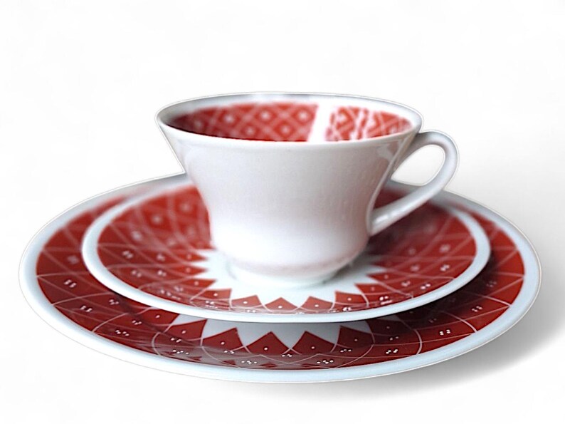 K&ouml;nnte beinhalten: Wei&szlig;es Teeservice mit Tasse, Untertasse und Teller. Das Innere der Tasse und die Oberfl&auml;chen von Untertasse und Teller weisen ein rotes geometrisches Muster auf. F&uuml;r Tee oder Kaffee.