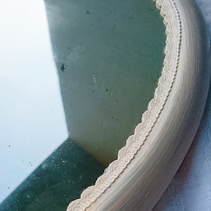 May include: A round mirror with a white painted wooden frame and a white crocheted trim around the edge.