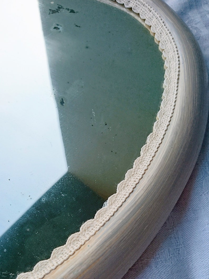 May include: A round mirror with a white painted wooden frame and a white crocheted trim around the edge.