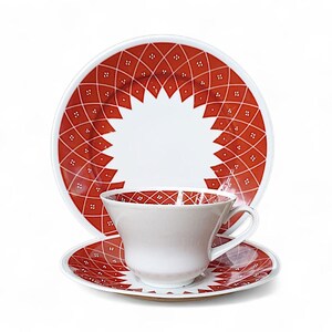 K&ouml;nnte beinhalten: Ein wei&szlig;es Tee-Set mit Tasse, Untertasse und Teller mit rotem geometrischem Muster. Das Muster zeigt ein Diamantgitter mit kleinen wei&szlig;en Punkten. Die Tasse und Untertasse haben das gleiche Design.