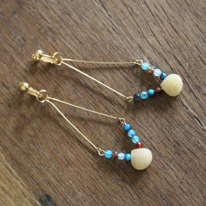 Può includere: Un paio di orecchini a clip dorati con una pietra bianca a forma di lacrima e perline blu e marroni.