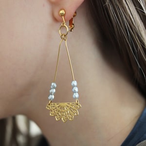 Può includere: Orecchini a clip dorati con un delicato design a forma di ventaglio e perline blu chiaro.