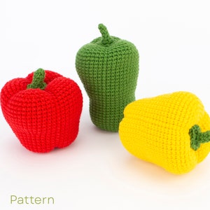 Puede incluir: Tres pimientos de crochet, uno rojo, uno verde y uno amarillo. Los pimientos están sobre una superficie blanca. La palabra "Pattern" está escrita debajo de los pimientos.