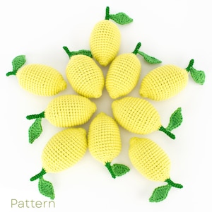 Puede incluir: Una disposición en forma de estrella de nueve juguetes de limón de ganchillo. Cada limón es amarillo con hojas verdes. Los limones están dispuestos en un círculo con las hojas apuntando hacia afuera. El fondo es blanco. Pattern.