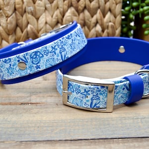 May include: Two blue waterproof dog collars featuring a white and blue seashell and starfish pattern. Each collar has a solid blue interior, a silver-toned metal buckle, a D-ring for leash attachment, and a silver metal rivet for secure adjustment.