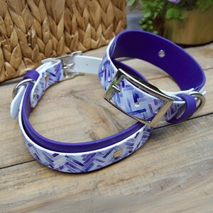 May include: Two dog collars, one white with a purple and white geometric pattern and a purple collar with a silver buckle.